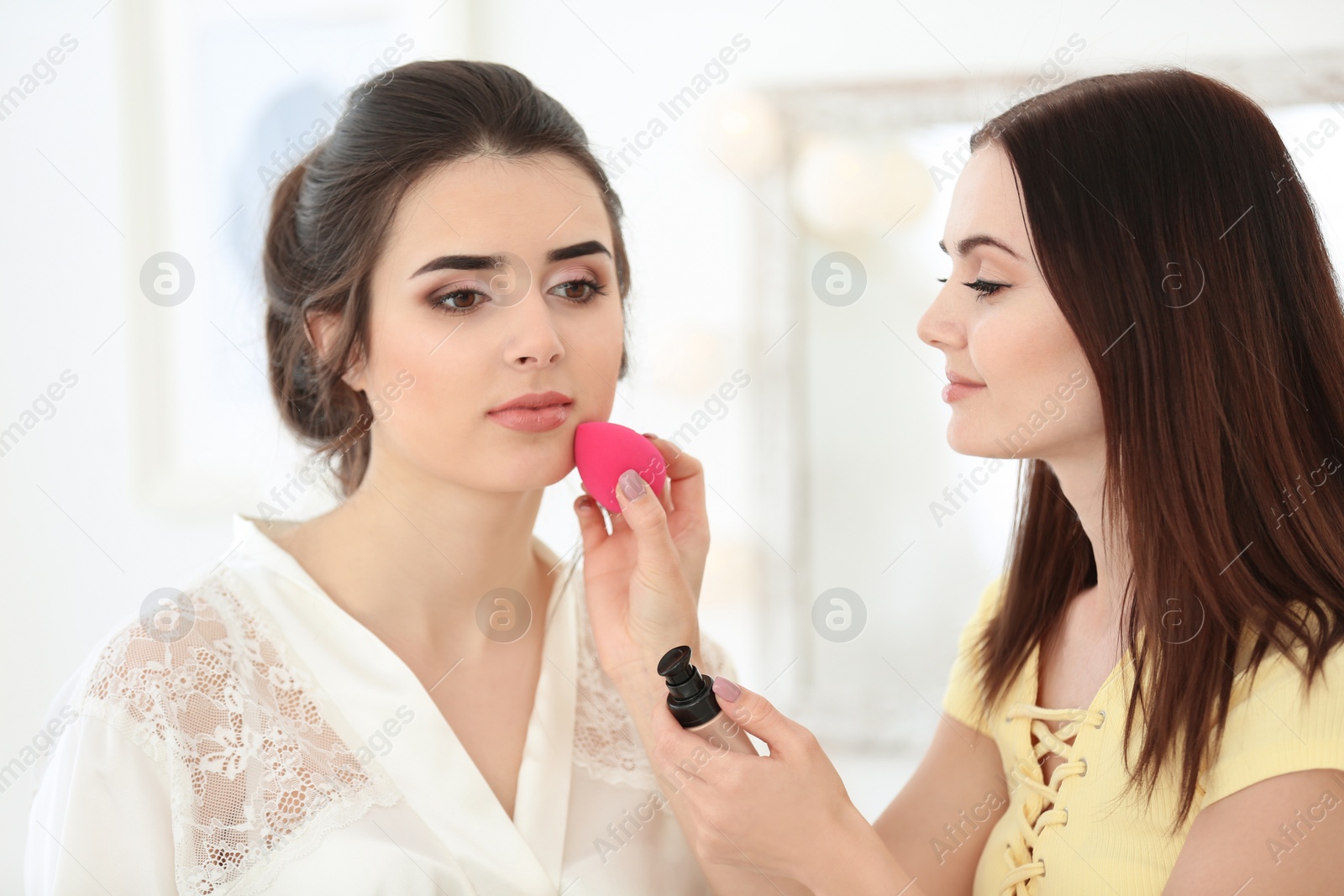 Photo of Professional makeup artist working with young woman in salon