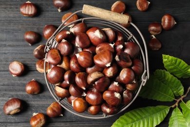 Photo of Fresh sweet edible chestnuts on black wooden  table, flat lay