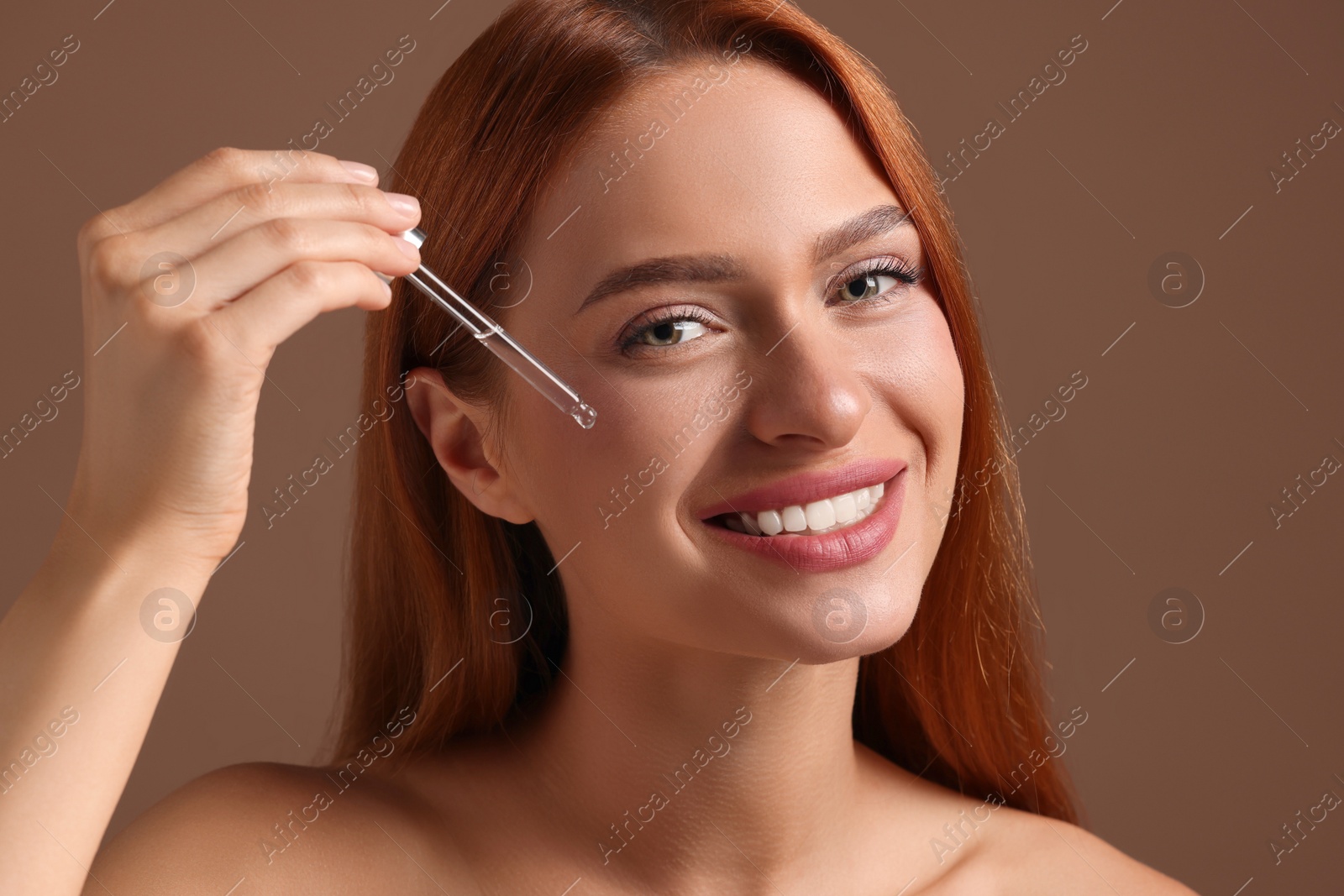 Photo of Beautiful young woman applying cosmetic serum onto her face on brown background, closeup