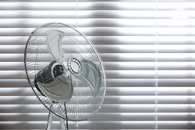 Photo of Modern electric fan near window indoors. Space for text