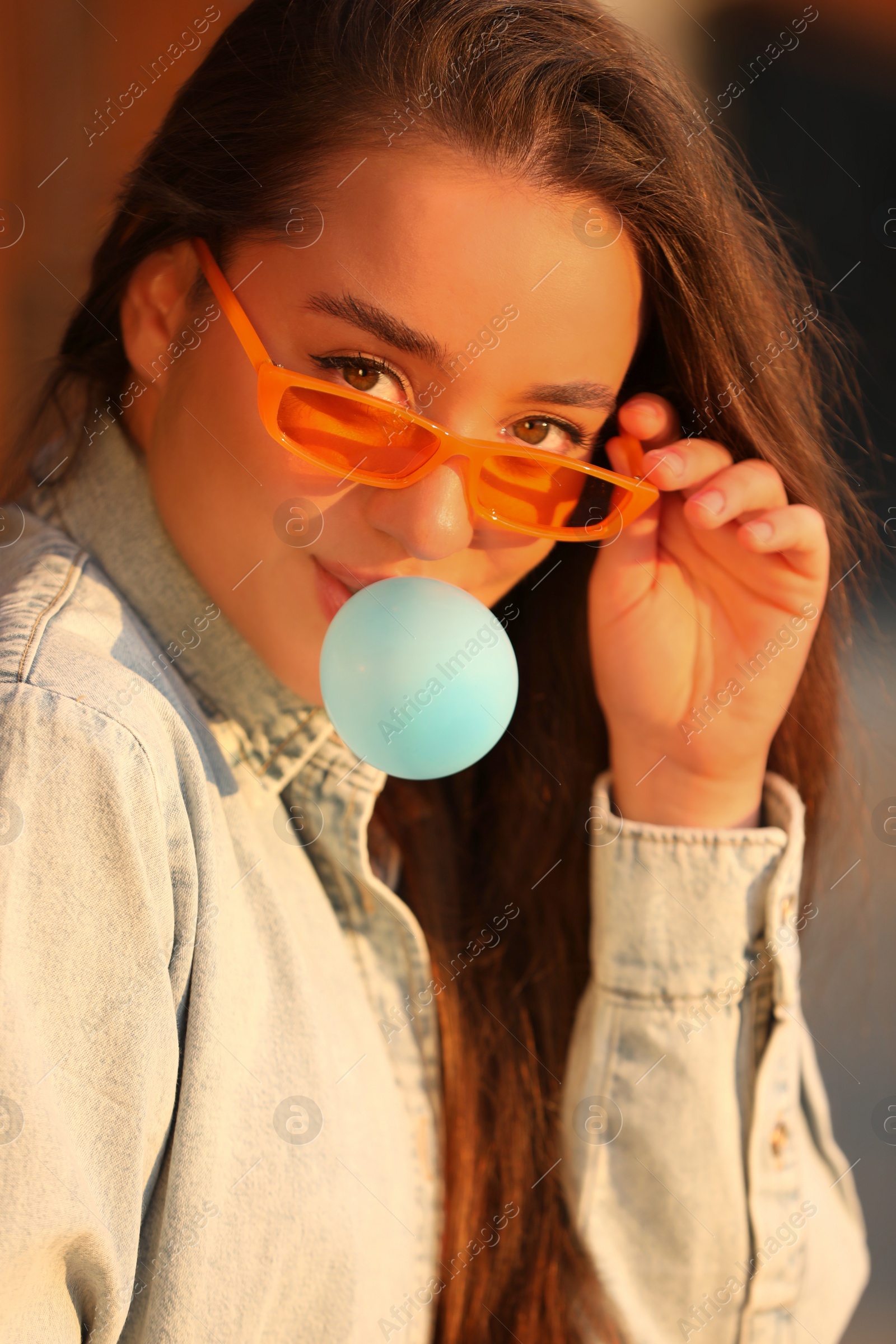 Photo of Beautiful young woman in sunglasses blowing bubble gum outdoors