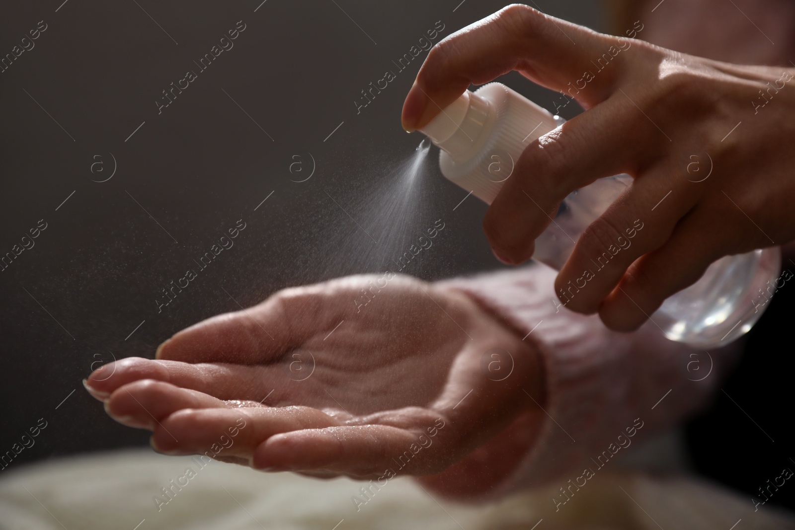 Photo of Woman spraying antiseptic onto hand against blurred background, closeup