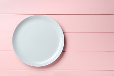 Photo of Clean white plate on pink wooden table, top view. Space for text