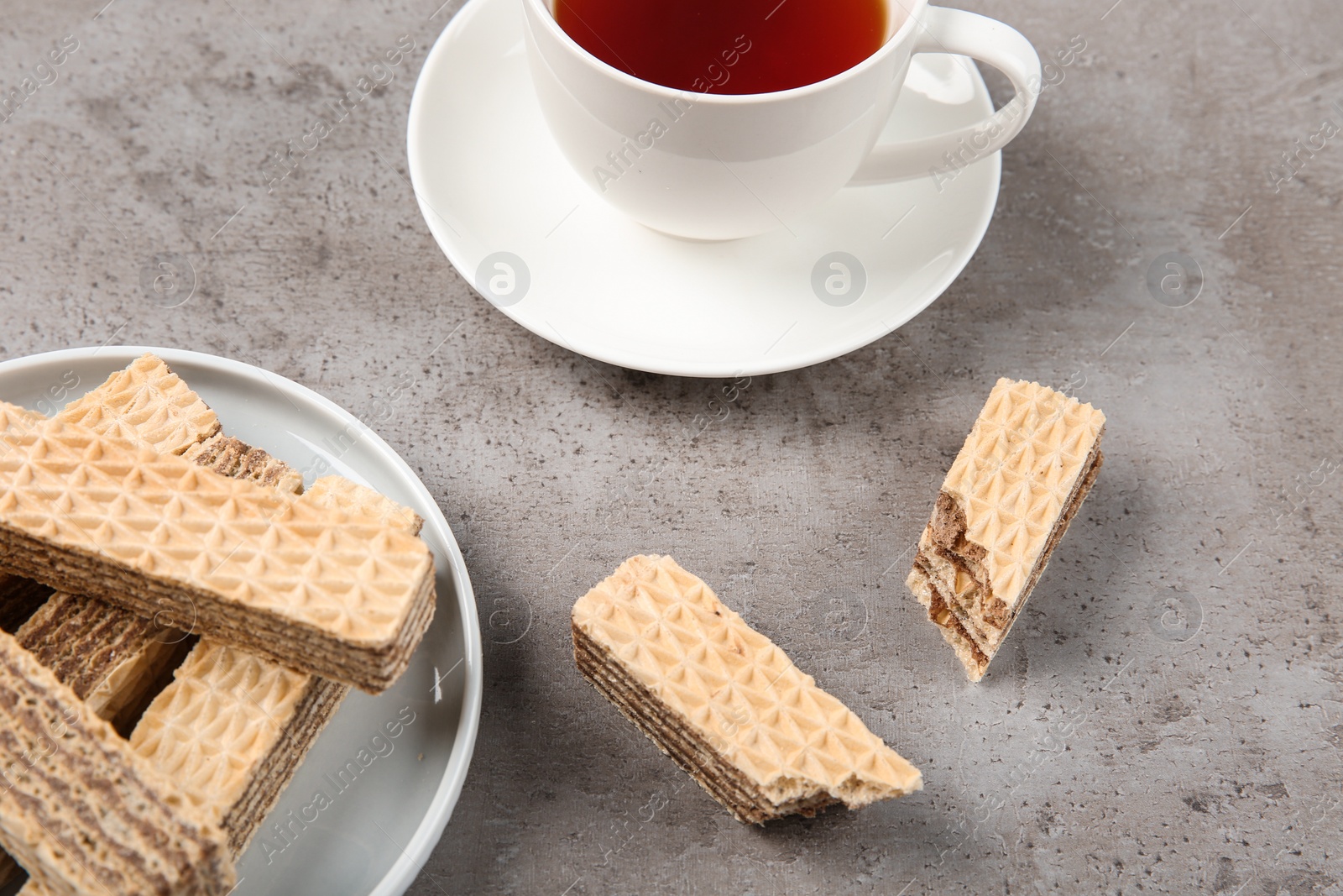 Photo of Plate of delicious wafers with cup of tea on grey stone background