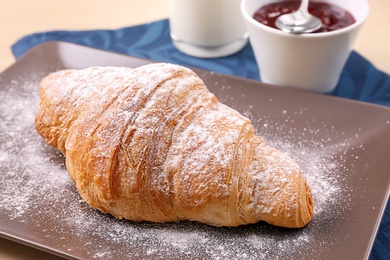 Photo of Tasty croissant with sugar powder on plate, closeup