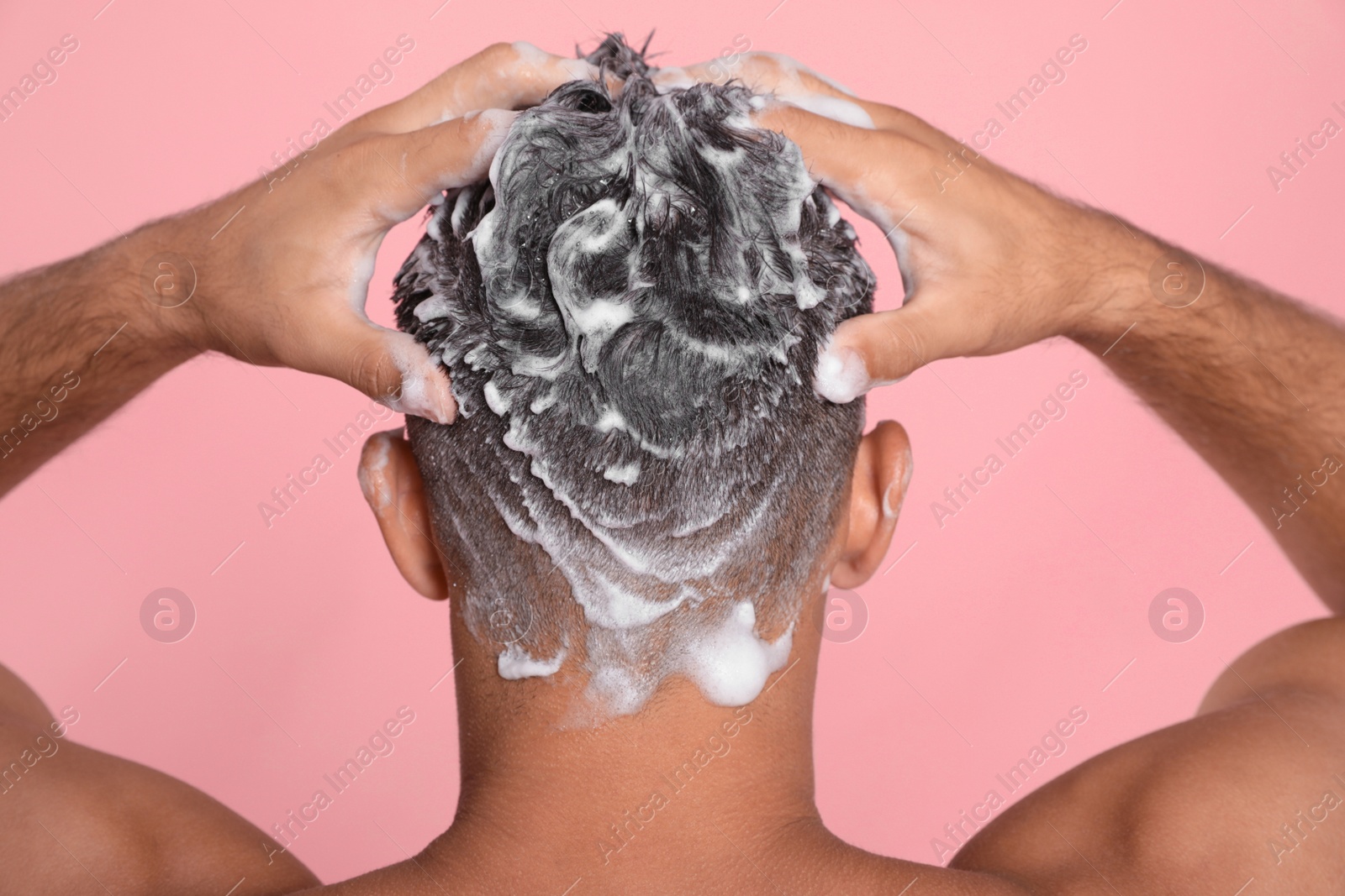 Photo of Man washing hair on pink background, back view