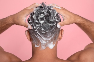 Man washing hair on pink background, back view
