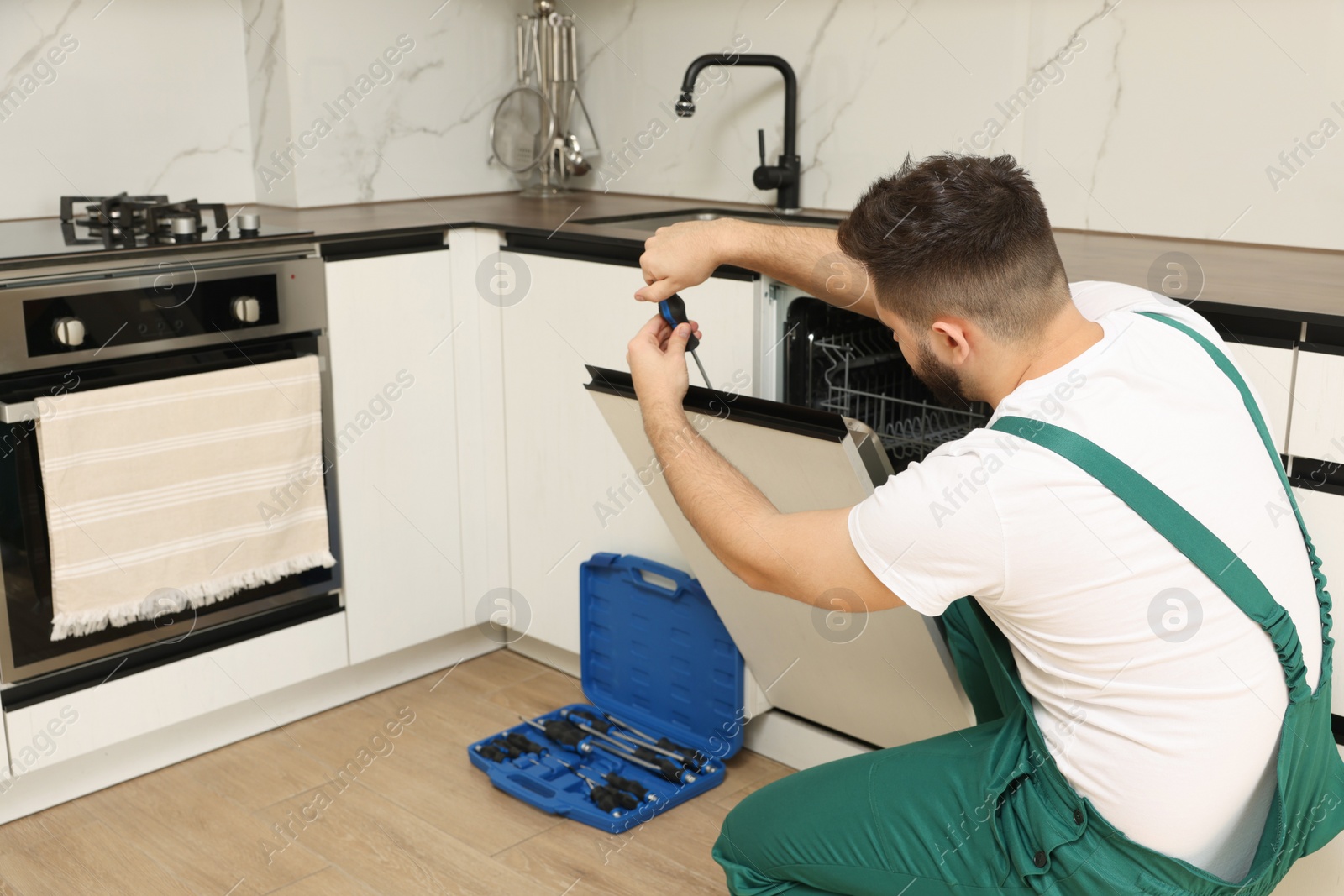 Photo of Serviceman repairing dishwasher door with screwdriver in kitchen