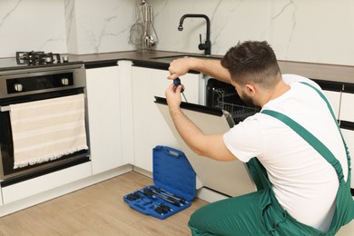 Serviceman repairing dishwasher door with screwdriver in kitchen