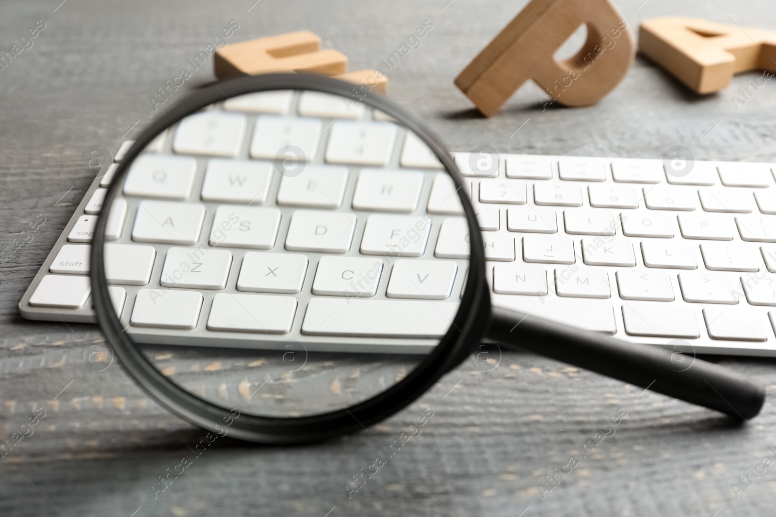 Photo of Magnifier glass, keyboard and letters on light grey wooden table, closeup. Find keywords concept