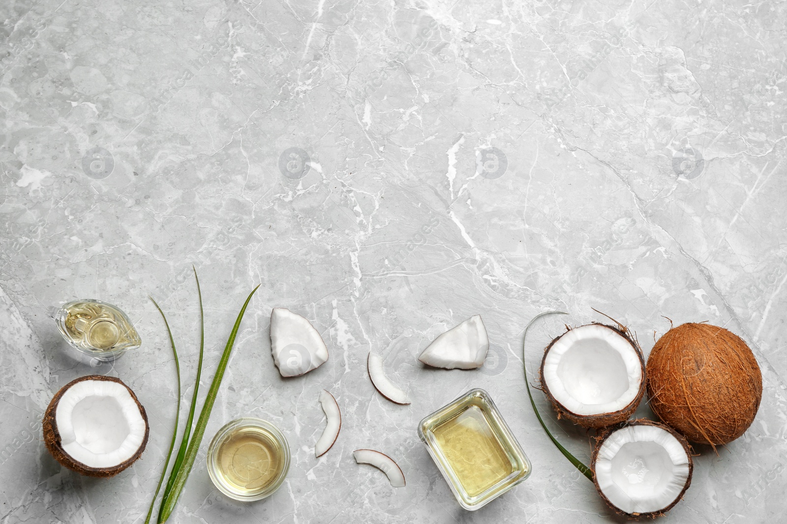 Photo of Glassware with natural organic oil and coconuts on grey stone background, flat lay. Space for text