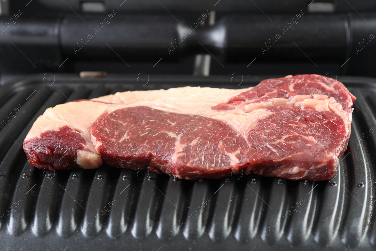 Photo of Cooking fresh beef cut on electric grill, closeup