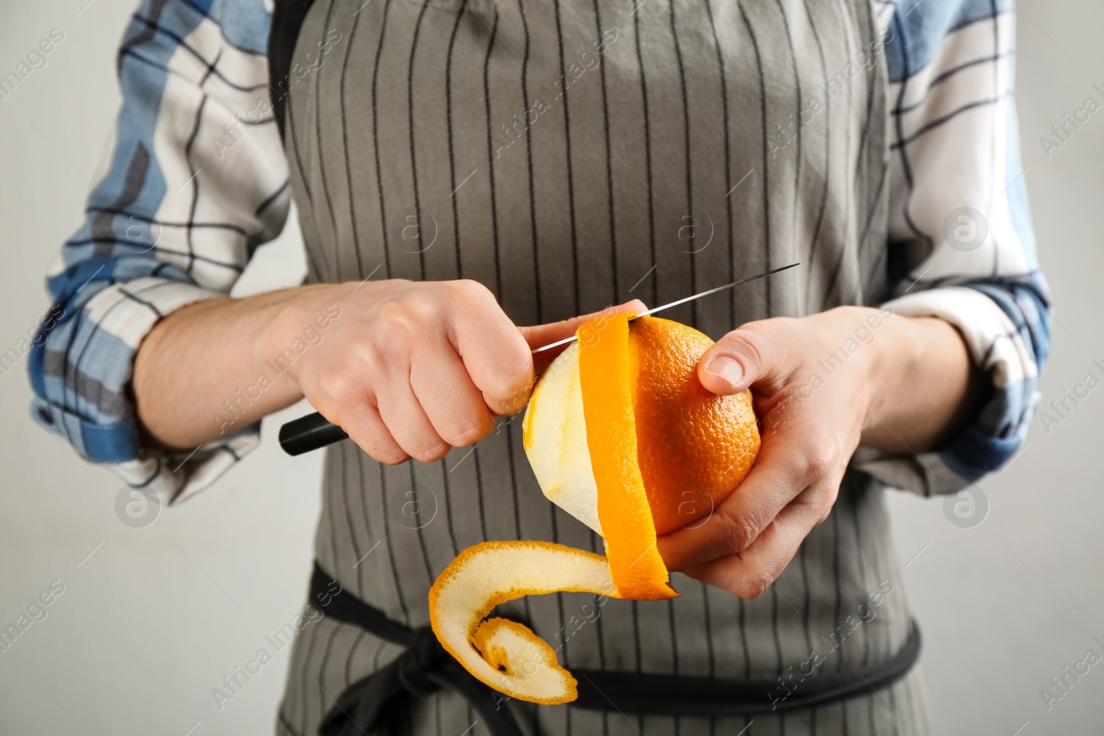 Photo of Woman peeling fresh orange with knife on light grey background, closeup