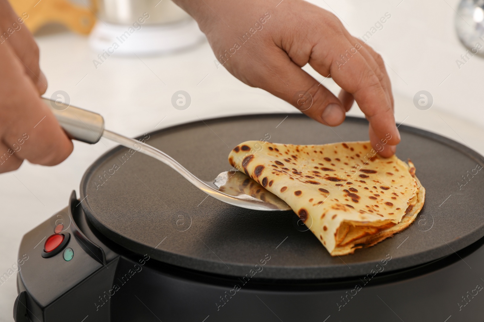 Photo of Man cooking delicious crepe on electric pancake maker at table, closeup