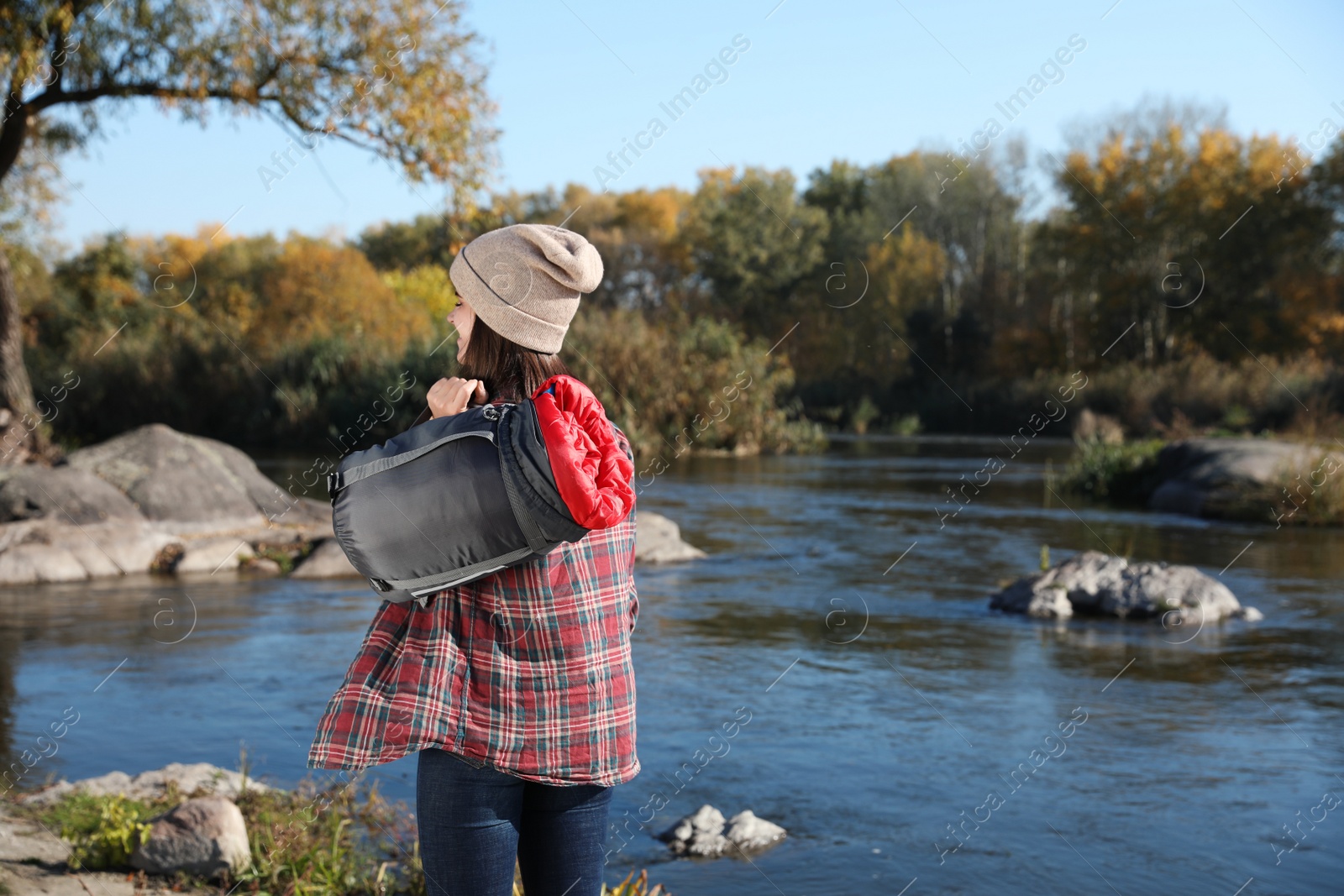 Photo of Female camper with sleeping bag near pond. Space for text