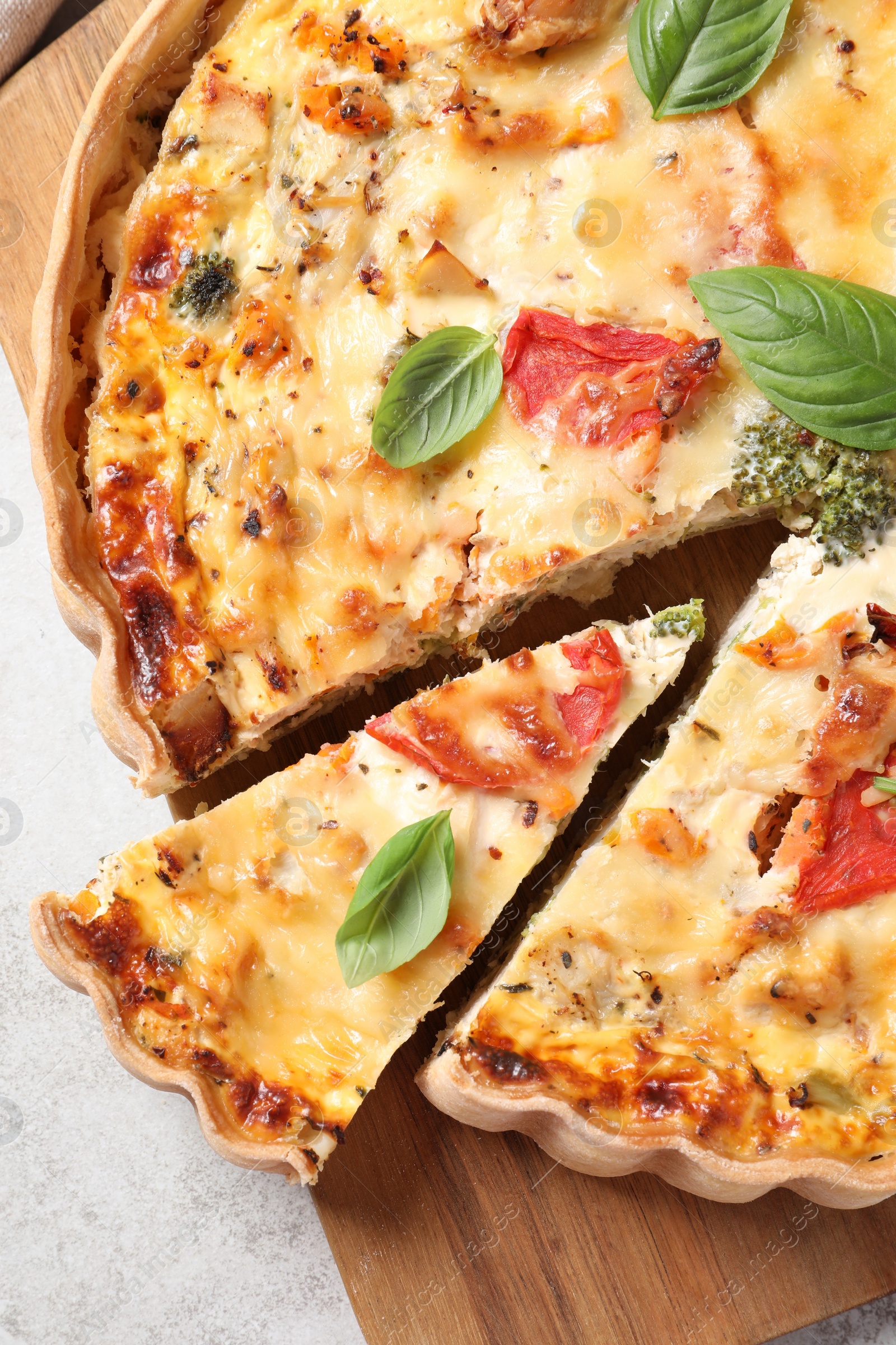 Photo of Tasty quiche with tomatoes, basil and cheese on light textured table, top view