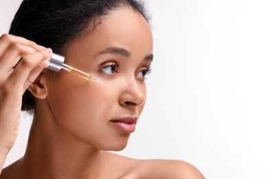 Photo of Beautiful woman applying serum onto her face on white background, closeup. Space for text