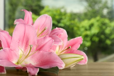 Photo of Beautiful pink lily flowers on wooden table, closeup. Space for text