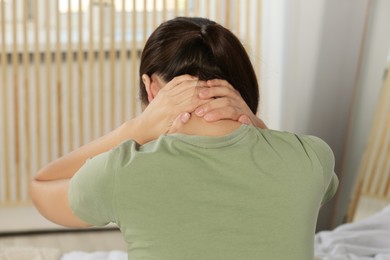 Photo of Young woman suffering from neck pain at home, back view