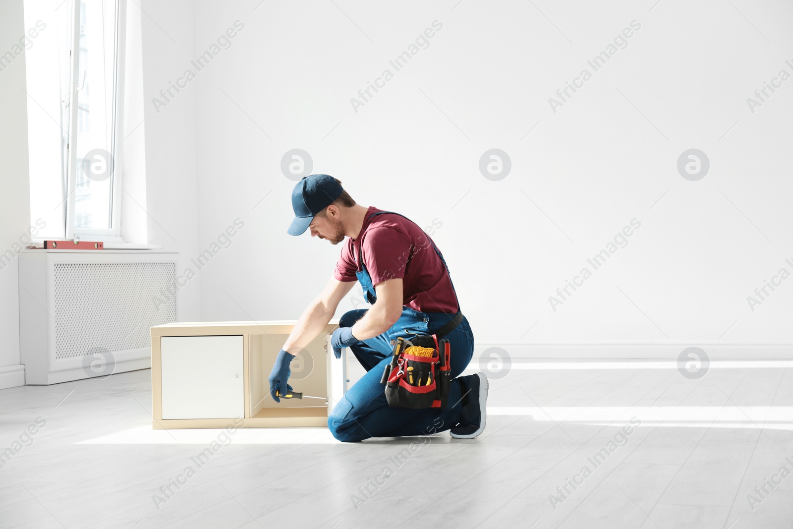 Photo of Handyman in uniform assembling furniture indoors, space for text. Professional construction tools