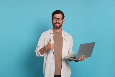 Photo of Handsome man with laptop showing thumb up gesture on light blue background