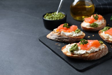 Photo of Delicious bruschettas with cream cheese, salmon and pesto sauce on black table, closeup. Space for text