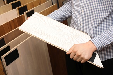 Photo of Man with sample of light wooden flooring in shop, closeup