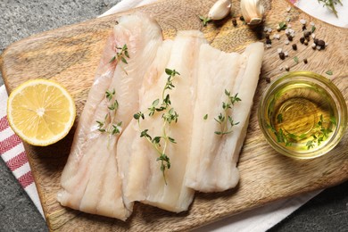 Photo of Raw cod fish, microgreens, lemon, oil and spices on grey textured table, top view