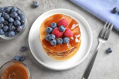 Tasty pancakes with fresh berries and syrup served on grey table, above view