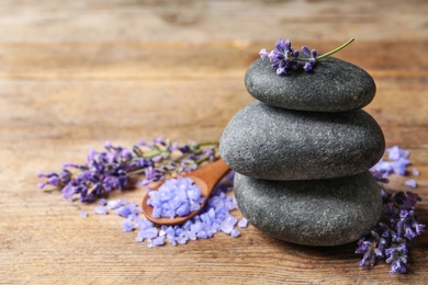 Spa stones, natural cosmetic bath salt and lavender flowers on wooden table, space for text