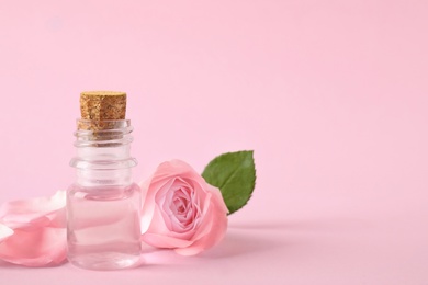 Bottle of essential oil and rose on pink background. Space for text