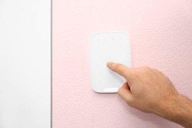 Young man entering code on alarm system keypad indoors, closeup