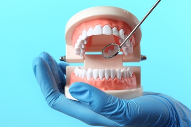 Photo of Dentist showing how to exam teeth with educational model of oral cavity and mouth mirror on color background