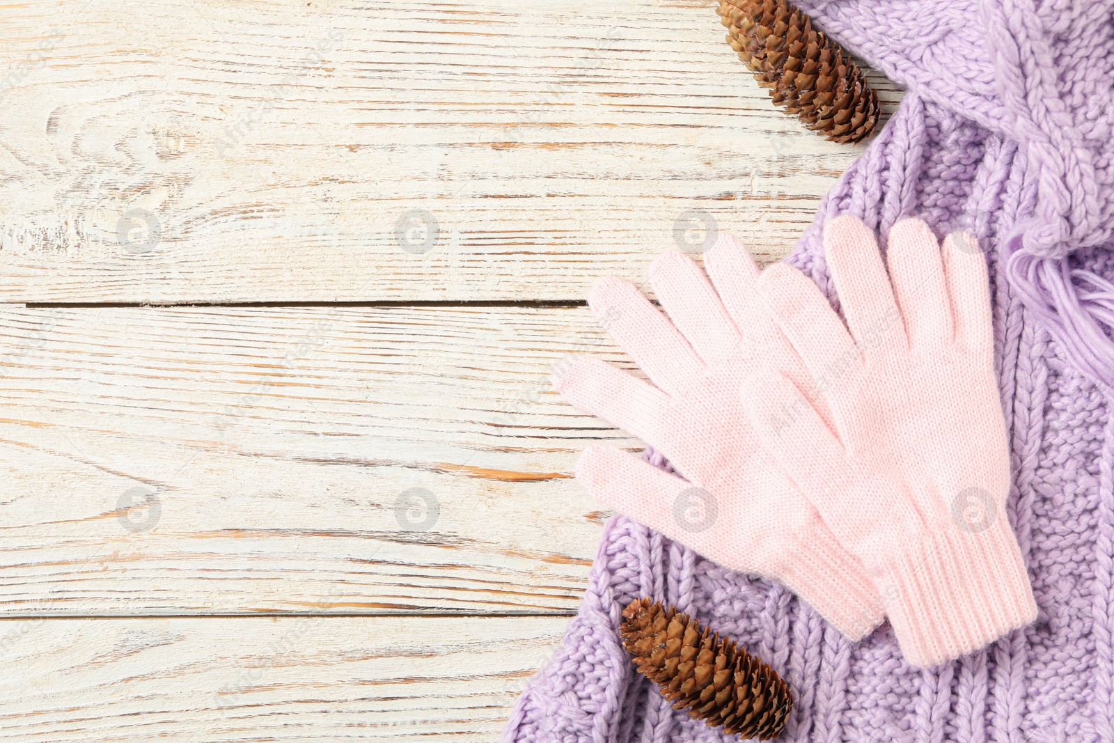 Photo of Stylish pink woolen gloves, scarf and fir cones on white wooden table, flat lay. Space for text