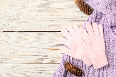 Stylish pink woolen gloves, scarf and fir cones on white wooden table, flat lay. Space for text