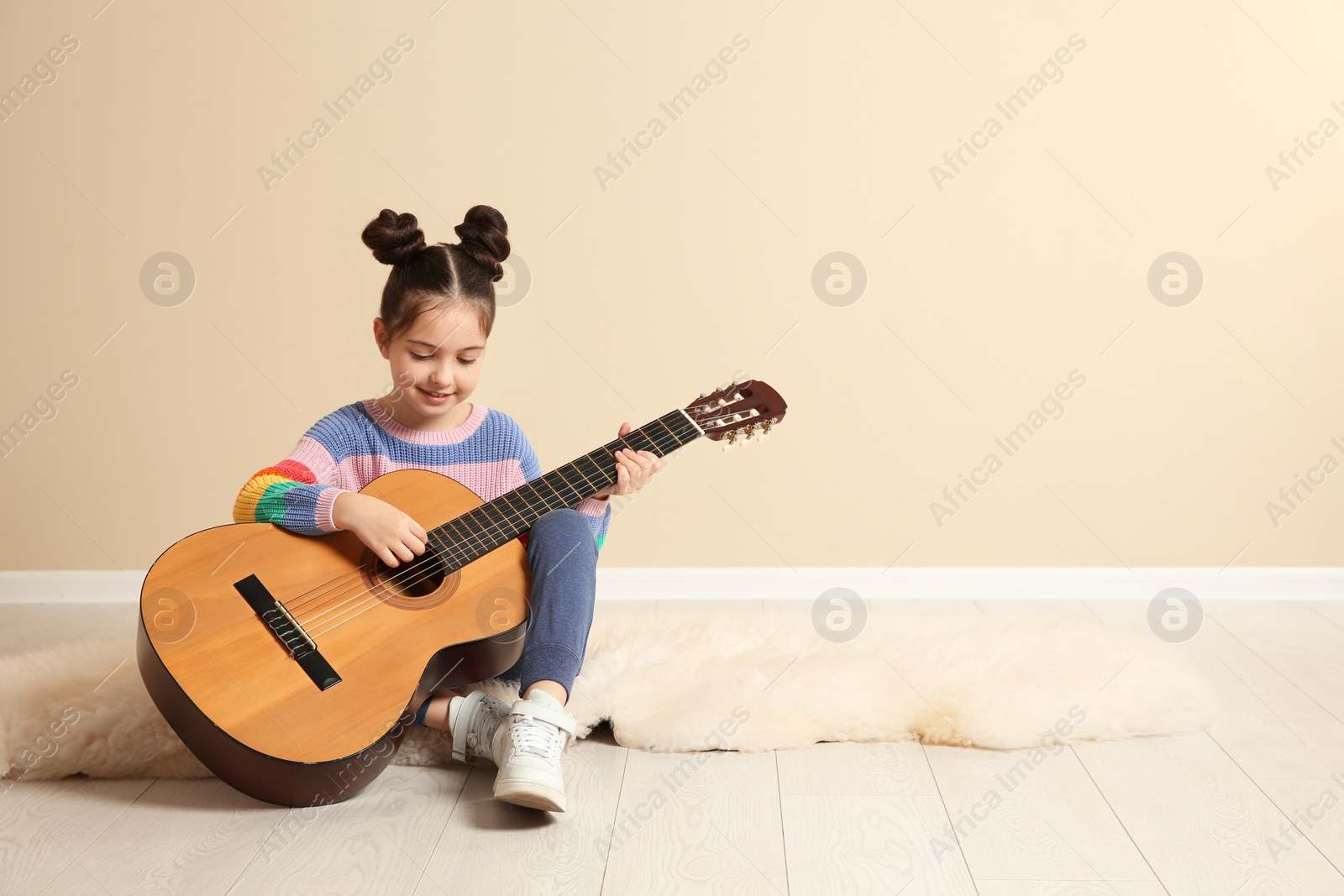 Photo of Cute little girl playing guitar on floor in room. Space for text