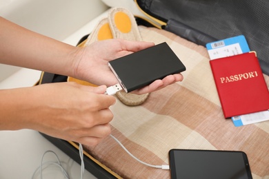 Woman charging smartphone with power bank near packed suitcase indoors, closeup