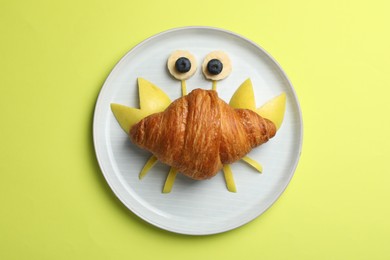 Funny crab made with croissant, fruits and berries on yellowish green background, top view
