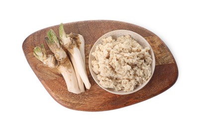 Photo of Wooden board with bowl of tasty prepared horseradish and roots isolated on white, top view