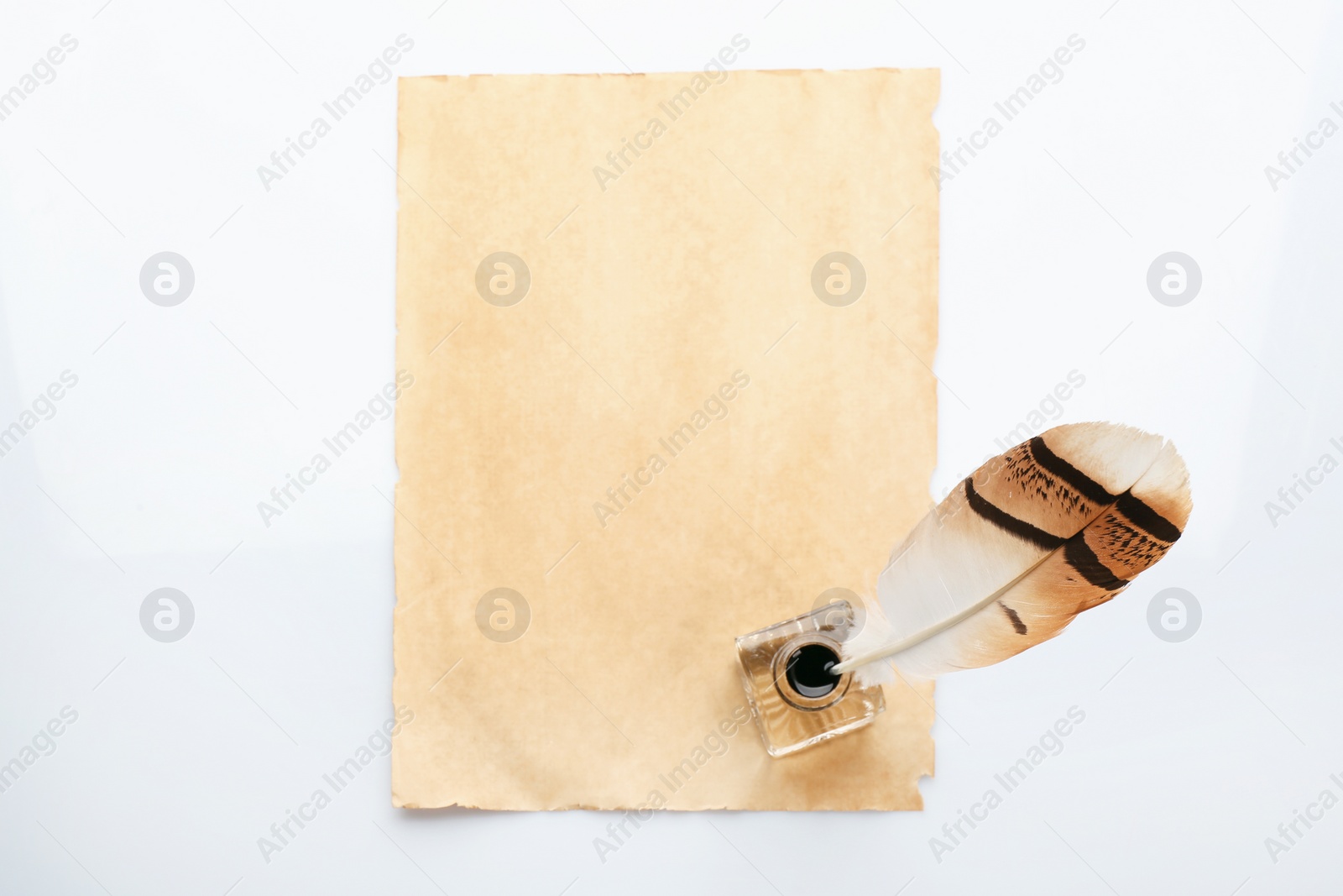 Photo of Feather pen with inkwell and blank paper on white background, top view. Space for text