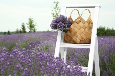 Photo of Wicker bag with beautiful lavender flowers on ladder in field, space for text
