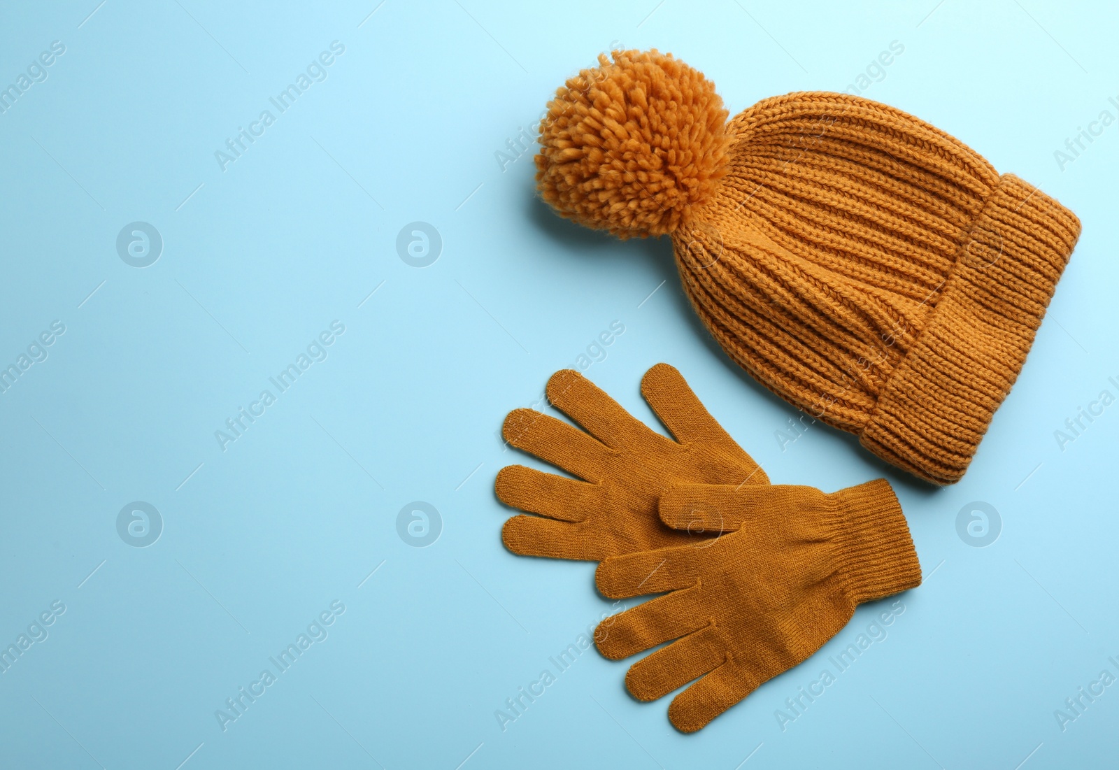 Photo of Woolen gloves and hat on light blue background, flat lay. Space for text