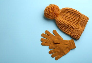 Woolen gloves and hat on light blue background, flat lay. Space for text