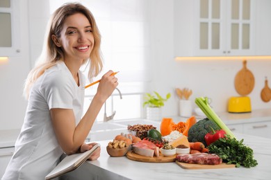 Woman with notebook and healthy food at white table in kitchen. Keto diet