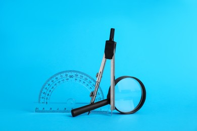 Photo of Protractor, magnifying glass and compass on light blue background