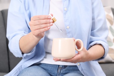 Photo of Woman dripping food supplement into cup indoors, closeup