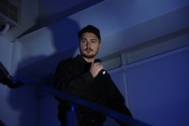 Photo of Male security guard with flashlight on stairs in darkness