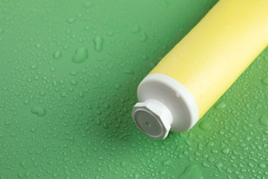 Moisturizing cream in tube on green background with water drops, closeup. Space for text