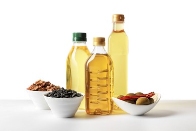 Photo of Bottles of different cooking oils, sunflower seeds, walnuts and olives on white background