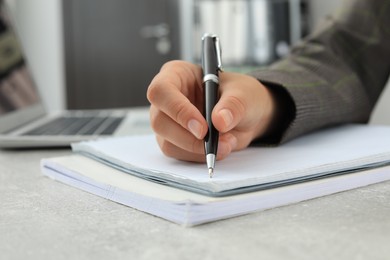 Woman writing in notebook at table indoors, closeup